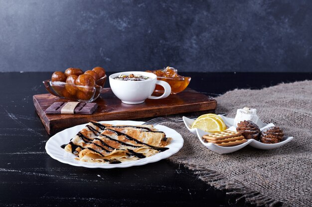 Crepes en un plato blanco con sirope de chocolate y té de hierbas.