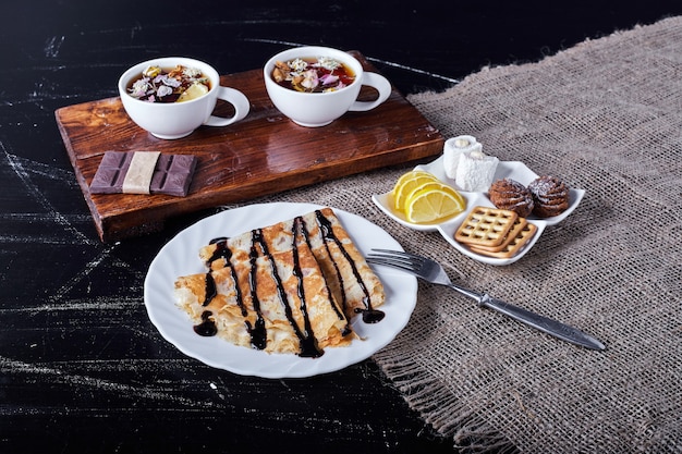 Foto gratuita crepes en un plato blanco con sirope de chocolate y té.