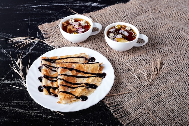 Crepes en un plato blanco con sirope de chocolate y té.