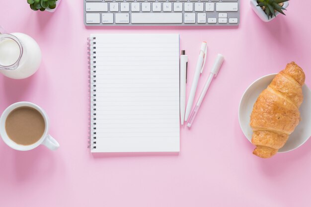 Croissant Al Horno taza de té Leche con teclado y suministros de oficina sobre fondo rosa