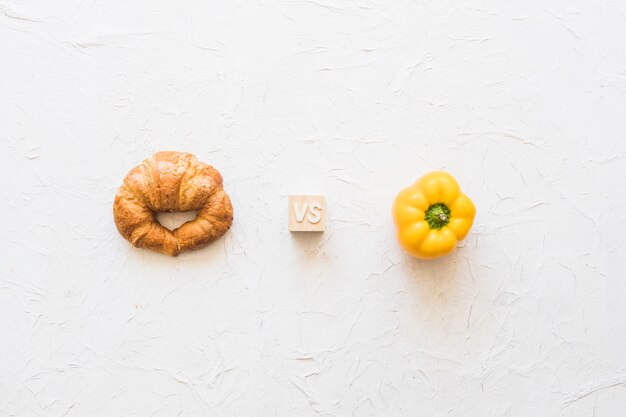 Croissant al horno versus bellpepper amarillo sobre fondo rugoso texturizado