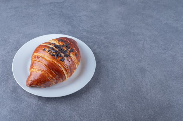 Croissant casero con chocolate en un plato, sobre el mármol.