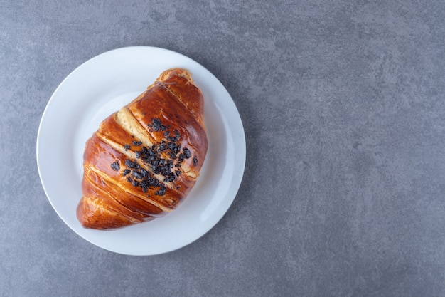 Croissant casero con chocolate en un plato sobre una mesa de mármol.