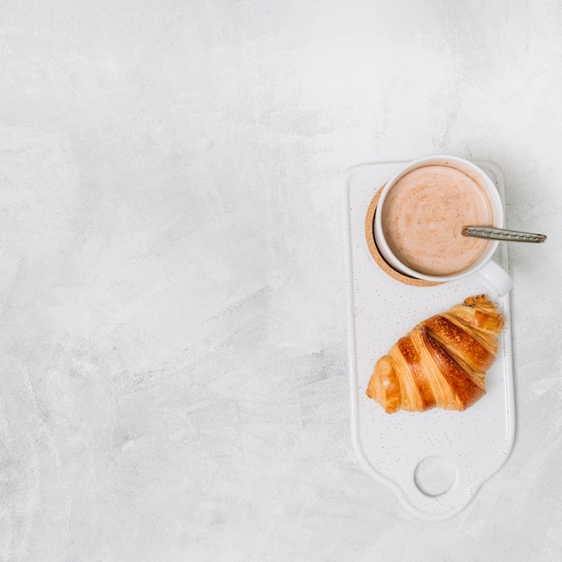 Croissant cerca de la taza de bebida en la tabla de cortar