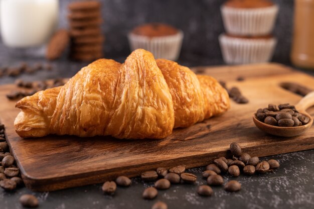 Croissant colocado sobre una plataforma de madera con granos de café sobre un piso de cemento negro.