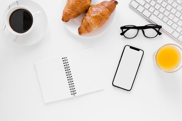 Croissant con cuaderno de café negro y teléfono inteligente