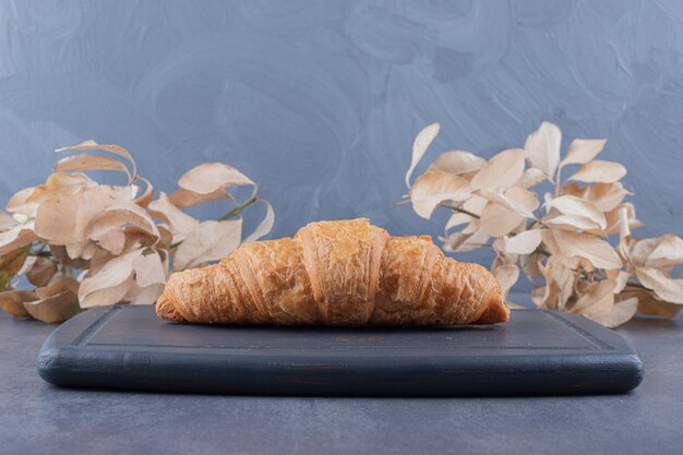 Croissant francés recién horneado sobre plancha de madera gris.