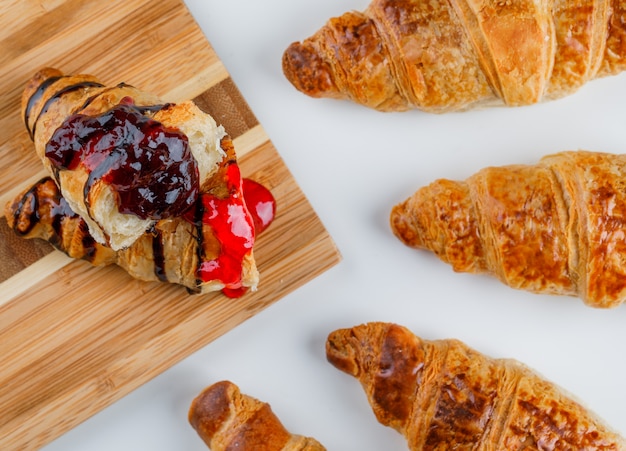 Croissant con mermelada en blanco y tabla de cortar, plano.