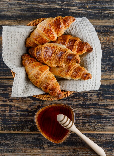 Croissant con miel, cazo en una cesta en la mesa de madera, plano.