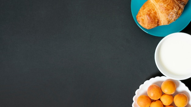 Croissant plano, leche y albaricoques sobre fondo liso con espacio de copia