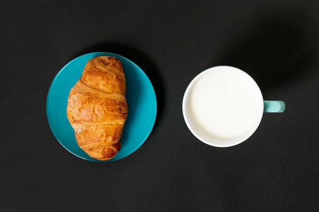 Croissant plano y taza de leche sobre fondo liso