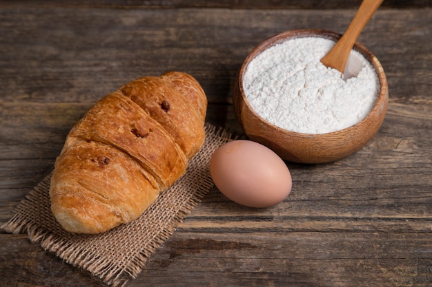 Croissant recién horneado con huevo de gallina marrón y harina colocados sobre una mesa de madera. Foto de alta calidad