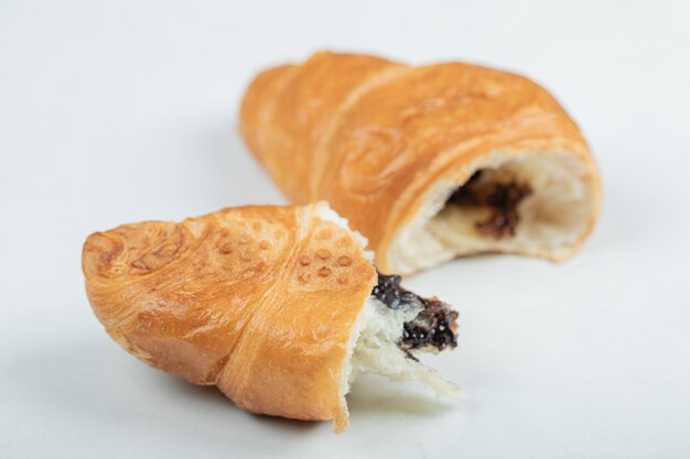 Croissant con relleno de chocolate sobre una superficie blanca.