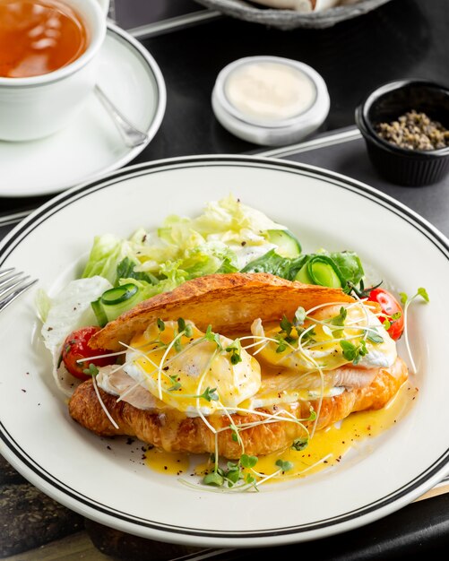 Croissant de salmón benedicto con huevo picado, salsa holandesa y servido con ensalada fresca