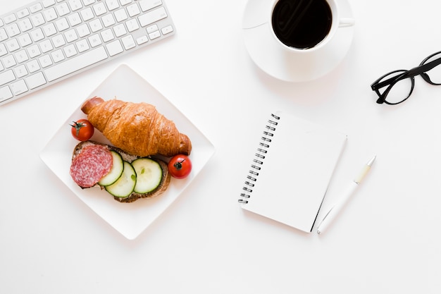 Croissant y sandwich en plato con café y cuaderno