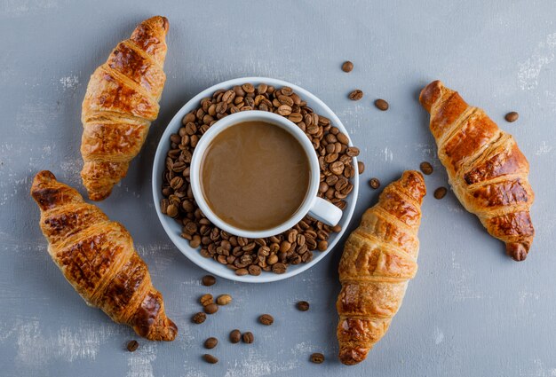 Croissant con taza de café, granos de café, plano.