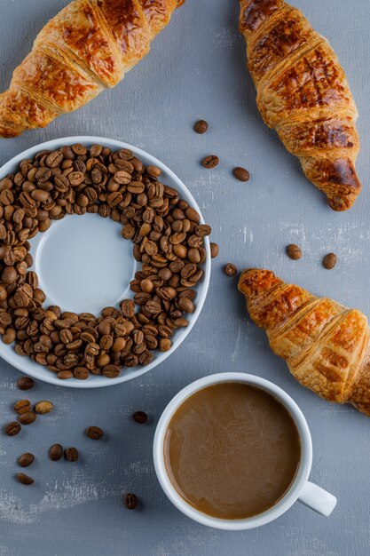 Croissant con taza de café, granos de café, plano.