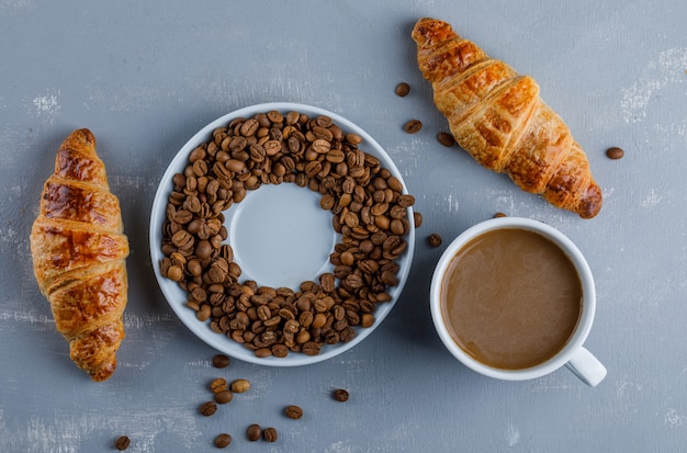 Croissant con taza de café, granos de café, plano.