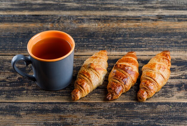 Croissant con taza de té de alto ángulo de vista sobre una mesa de madera