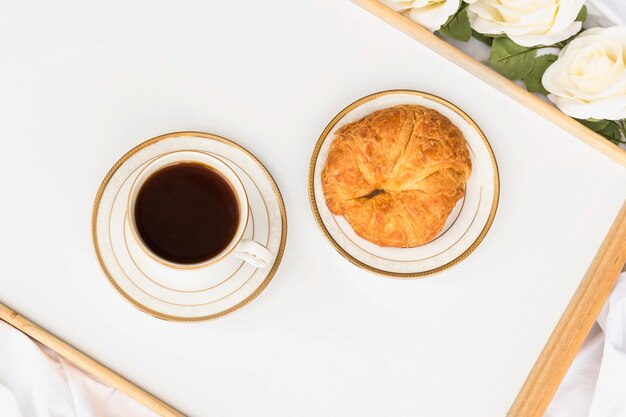 Croissant con taza de té en bandeja de madera