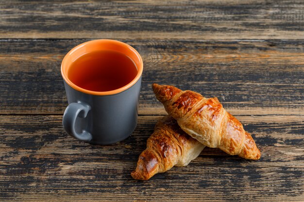 Croissant con taza de té en la mesa de madera, vista de ángulo alto.