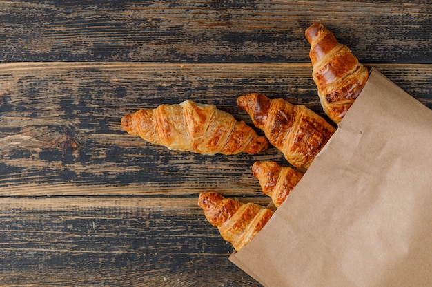 Croissants en una bolsa de papel sobre una mesa de madera. aplanada