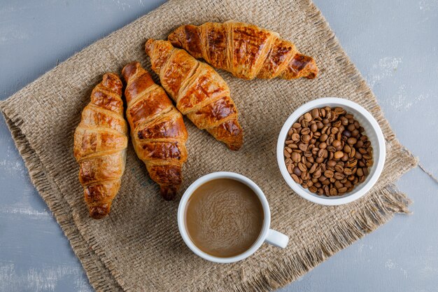 Croissants con café y frijoles sobre yeso y saco, plano.