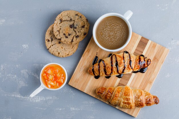 Croissants con café, galletas, salsa plana sobre yeso y tabla de madera.