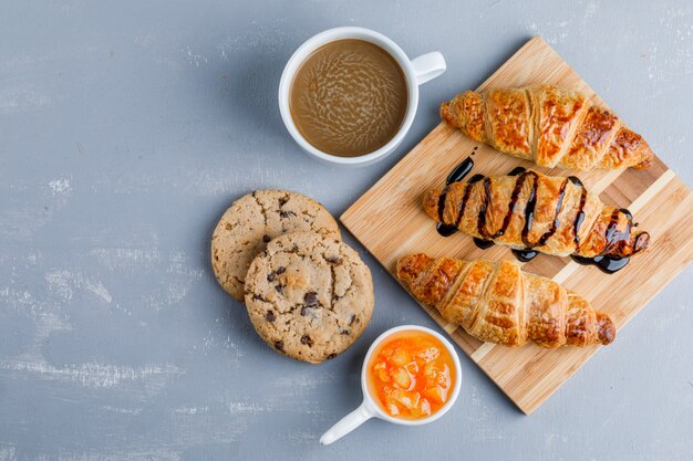 Croissants con café, galletas, salsa plana sobre yeso y tabla de madera.