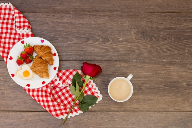 Croissants con café y rosa roja.