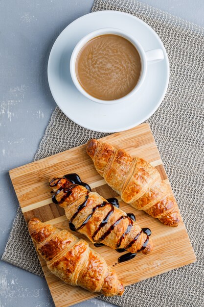 Croissants con café, tabla de cortar, plano.