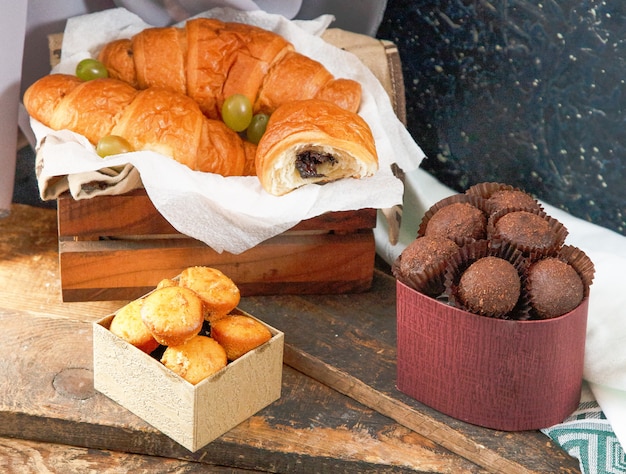 Croissants de chocolate, caja de bombones y muffins en un trozo de madera