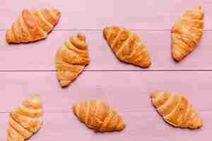 Foto gratuita croissants esparcidos sobre mesa rosa