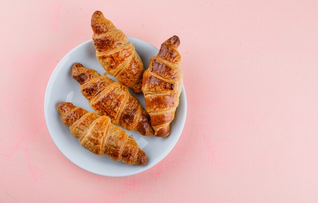 Croissants en un plato blanco sobre una mesa de color rosa. aplanada