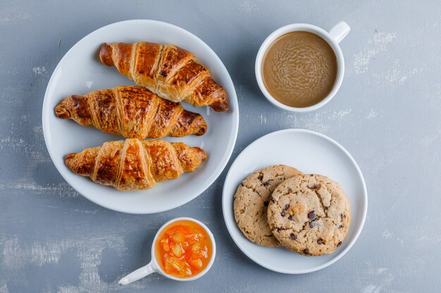 Croissants en un plato con taza de café, galletas, mermelada, vista superior