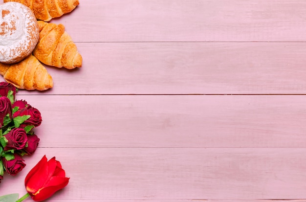 Croissants con ramo de rosas en mesa rosa