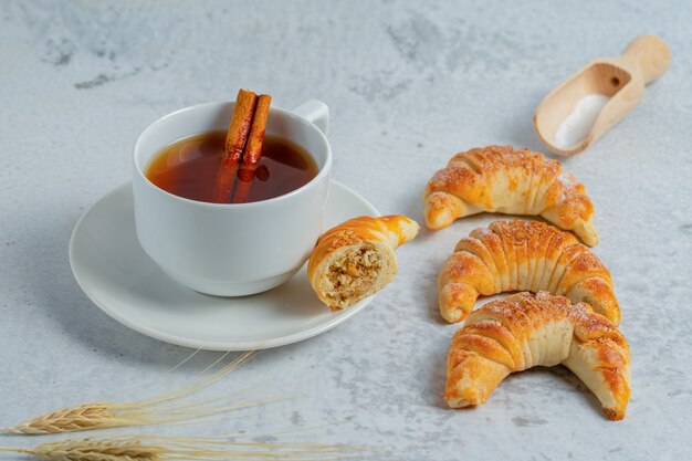 Croissants recién hechos con té fragante en superficie gris.