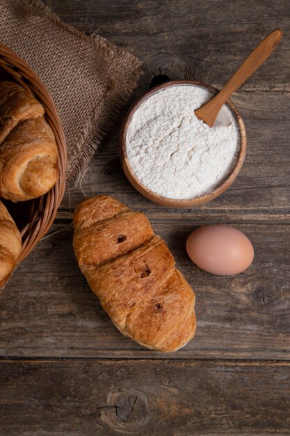 Croissants recién horneados con huevo de gallina marrón y harina colocados sobre una mesa de madera. Foto de alta calidad