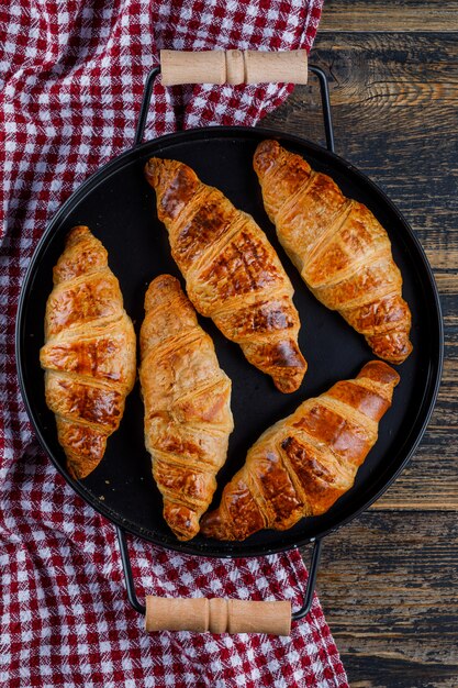 Croissants en una sartén de madera y papel de cocina. aplanada