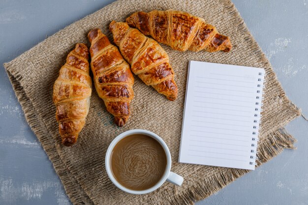 Croissants con taza de café, cuaderno plano sobre yeso y saco