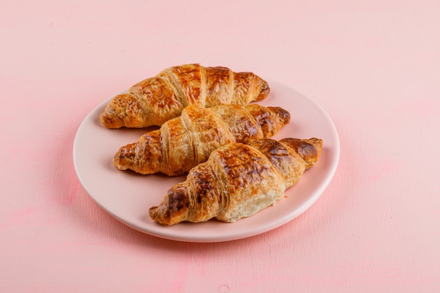 Croissants en una vista de ángulo alto de placa sobre una mesa rosa