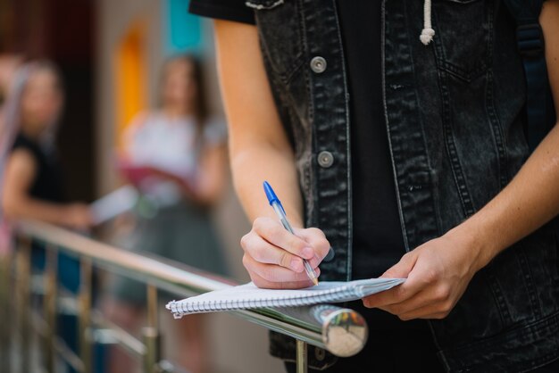 Crop estudiante de escribir en el bloc de notas