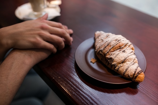 Crop pareja de la mano cerca de croissant