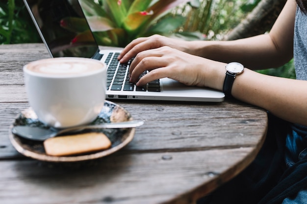 Crop persona que usa la computadora portátil cerca del café