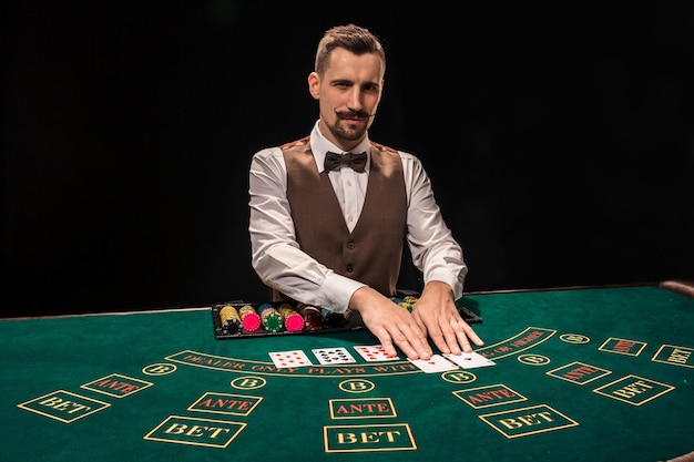 Croupier detrás de la mesa de juego en un casino sobre fondo negro. El concepto de victoria.