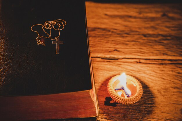 Cruce con la Santa Biblia y la vela en una vieja mesa de madera de roble.