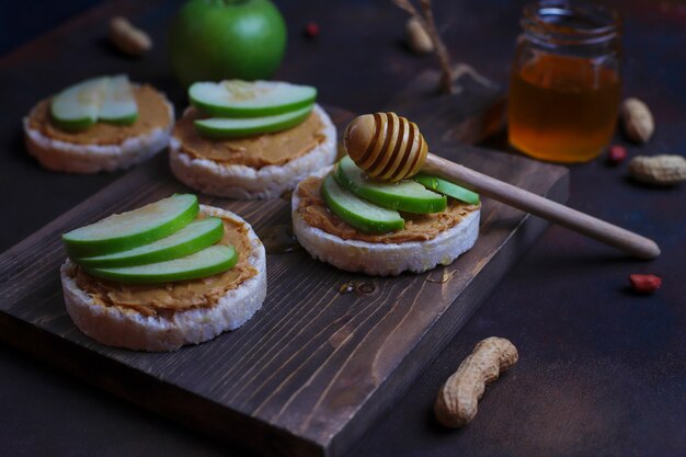 Crujiente sándwich de mantequilla de maní natural con pan de pastel de arroz y rodajas de manzana verde y miel.