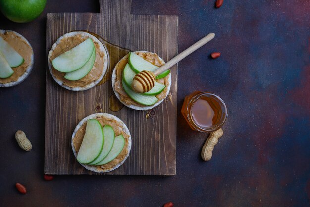 Crujiente sándwich de mantequilla de maní natural con pan de pastel de arroz y rodajas de manzana verde y miel.