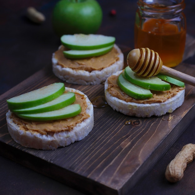 Crujiente sándwich de mantequilla de maní natural con pan de pastel de arroz y rodajas de manzana verde y miel.