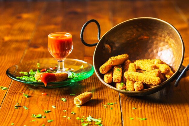 Crujientes dedos de pollo en utensilio de cobre con salsa en la mesa de madera
